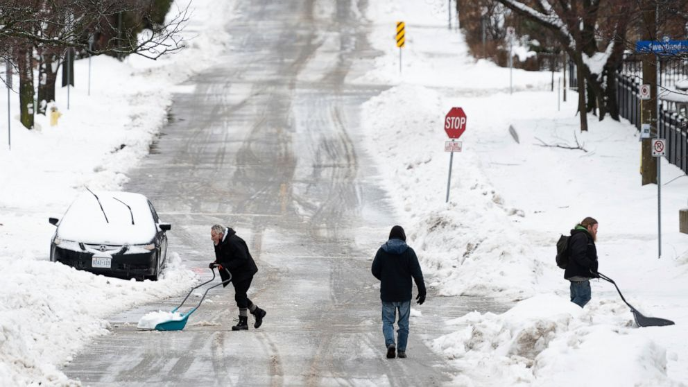 People shovel snow in the Sandy Hill neighborhood of Ottawa, on Friday, Dec. 23, 2022. Environment Canada has issued a winter storm warning for the region which is calling for flash freezing, icy and slippery surfaces, wind gusts and chills. (Spencer